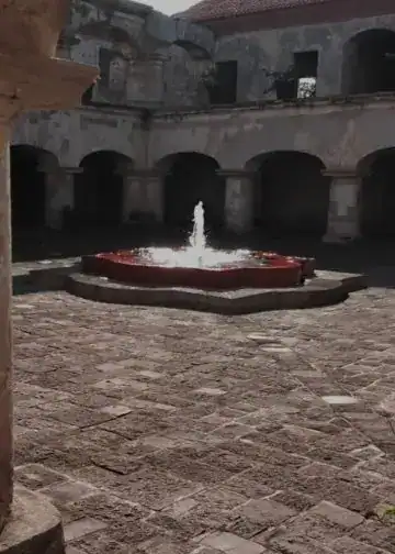 La prisión ya solo es un recuerdo. El proceso de restauración sigue en marcha a cargo del Consejo Nacional para la Protección de Antigua Guatemala (Foto Gustavo Montenegro) – SoyMigrante.com REVISTA Fuente en el centro de la terraza con fuente de agua en un patio histórico. Edificio colonial con arcos y paredes de piedra, ambiente tranquilo y clásico en el interior de un edificio antiguo.