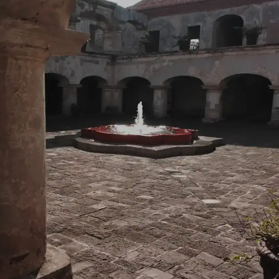 Fuente en el centro de la terraza con fuente de agua en un patio histórico. Edificio colonial con arcos y paredes de piedra, ambiente tranquilo y clásico en el interior de un edificio antiguo. – SoyMigrante.com REVISTA