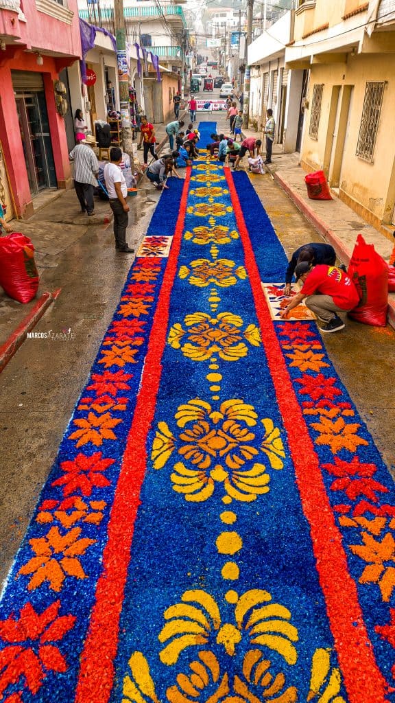 Las calles se convierten en ofrenda de símbolos ancestrales florecientes – SoyMigrante.com REVISTA Colorido mosaico de flores preparado para una celebración tradicional en una calle de ciudad mexicana. Personas participando en la elaboración del tapete artesanal, tradición cultural importante en festividades. – SoyMigrante.com REVISTA