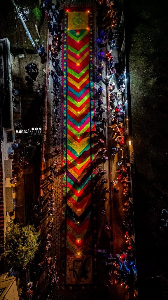 Como dijimos antes: las calles hablan sin palabras y las alfombras indican el camino de todos: ser ofrenda efímera porque la vida es corta. – SoyMigrante.com REVISTA Coloquio con velas y flores en honor a la cultura y tradiciones mexicanas en celebración del Día de los Muertos en la ciudad. Evento cultural con comunidad participando en ofrenda decorativa colorida y vibrante. – SoyMigrante.com REVISTA