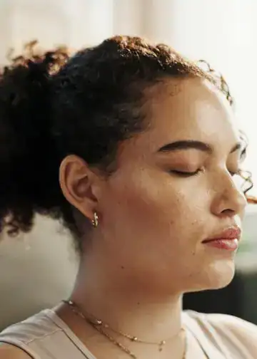 SoyMigrante.com REVISTA: Mujer con rostro relajado y ojos cerrados, disfrutando un momento de calma en su ambiente cotidiano, representando tranquilidad, bienestar y empoderamiento femenino en contexto de migración y diversidad. – SoyMigrante.com REVISTA