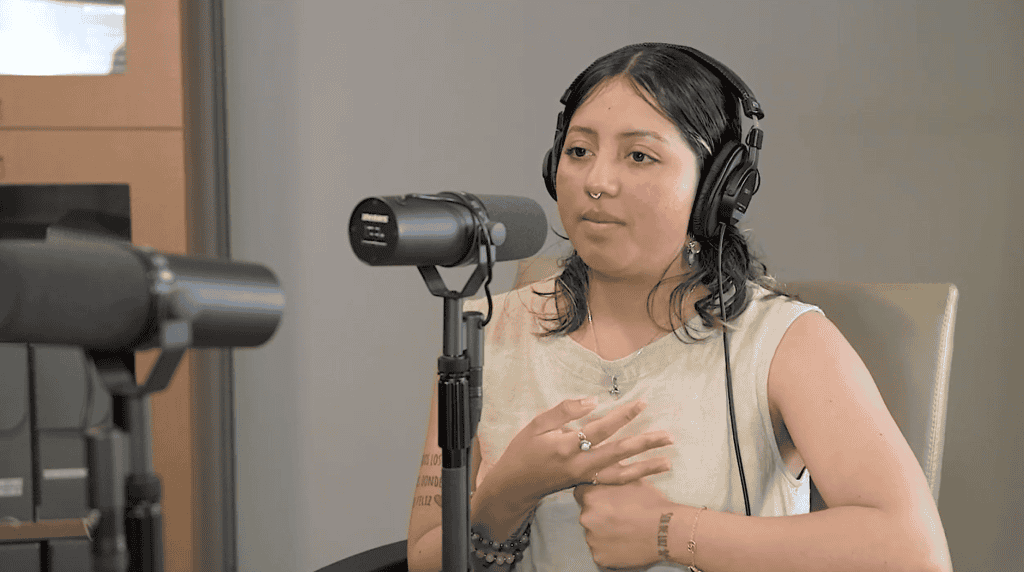 Joven mujer con cabello oscuro, auriculares y piercings, grabando un podcast o entrevista en un estudio de radio. – SoyMigrante.com REVISTA