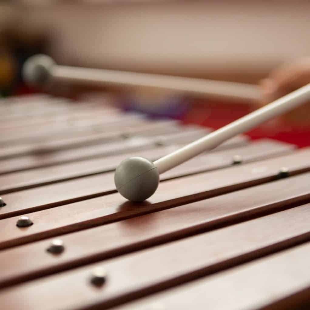 Mecanismo de xilófono, instrumento musical tradicional, enfoque en las barras de madera y la maza, ideal para artículos sobre cultura, música y la comunidad latina en la revista SoyMigrante.com REVISTA.