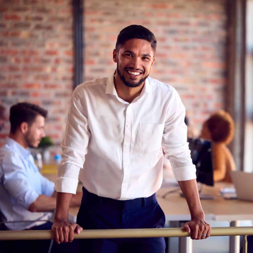 Joven profesional sonriente en oficina moderna, inspirando éxito y liderazgo en el trabajo. – SoyMigrante.com REVISTA