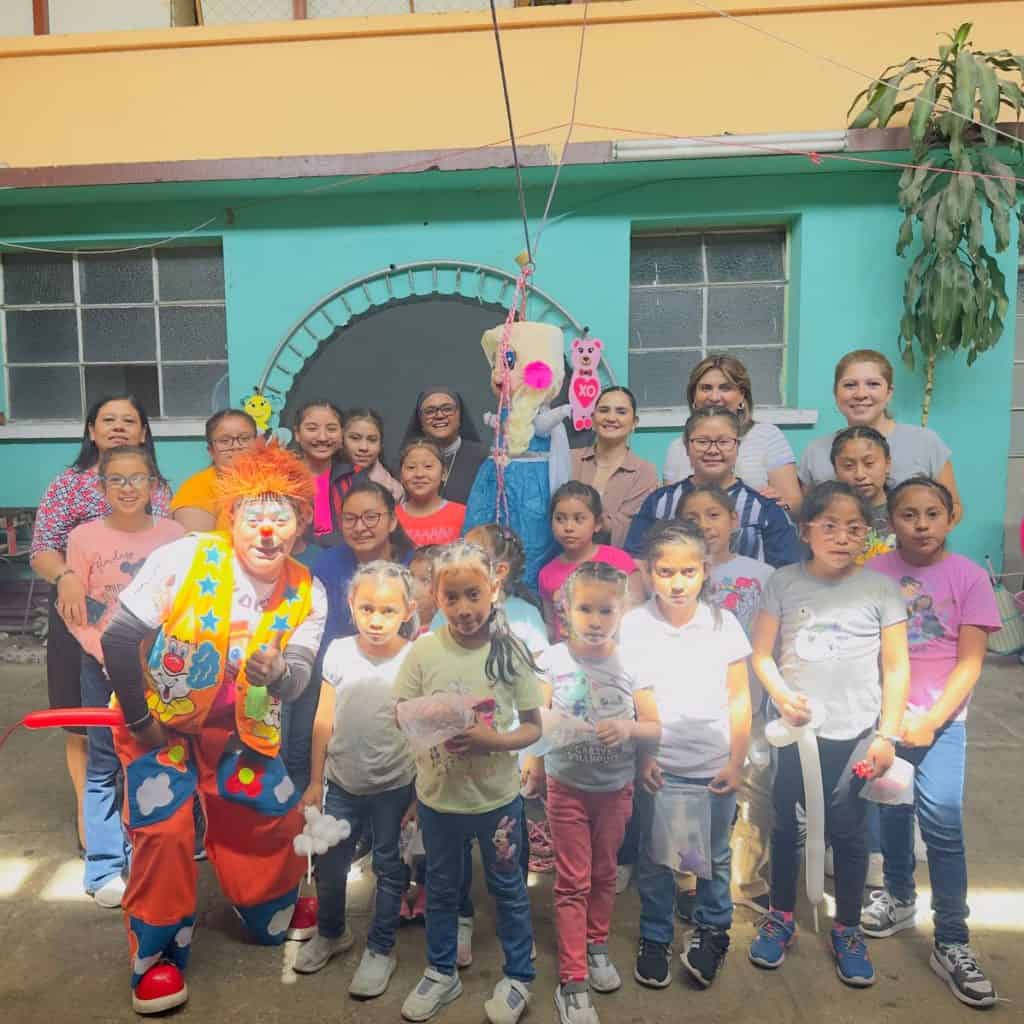Muñecos de payaso y marionetas en celebración infantil en comunidad escolar, niños y maestras participan en actividades recreativas y culturales para promover alegría y convivencia.