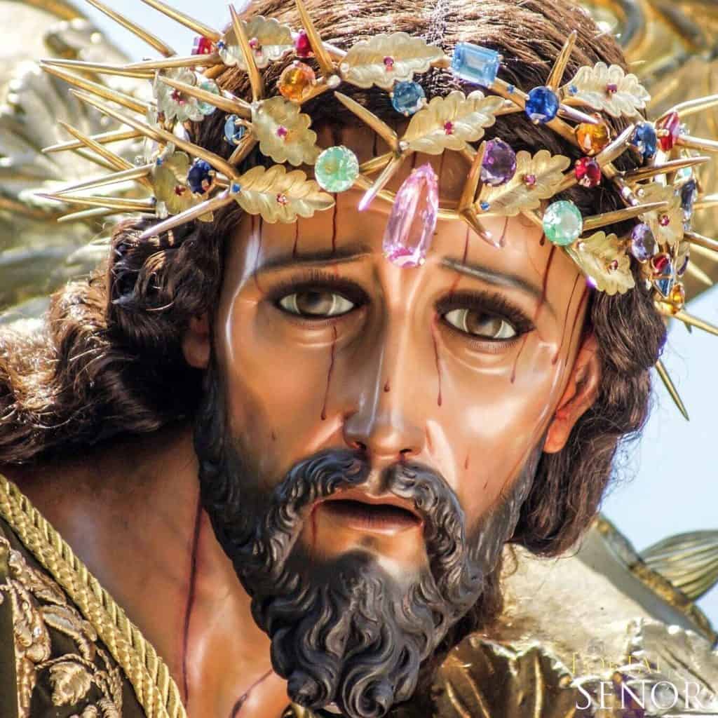 Relieve de un Cristo con corona de espinas decorada con joyas y cristales, representando la pasión y el sufrimiento, en la portada de la revista SoyMigrante.com REVISTA.