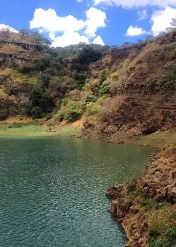 Laguna natural rodeada de montañas con vegetación, paisaje pintoresco en un entorno tranquilo y soleado.