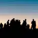 Personas migrantes en reunión al atardecer, siluetas en un entorno social, resaltando temas de migración, comunidad y cultura en la revista SoyMigrante.com REVISTA.