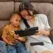 Mamás migrantes usando tableta y móvil con hijo niño pequeño en casa, tecnología y familia, comunicación y educación en el hogar, contenido de SoyMigrante.com REVISTA.