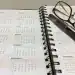 Calendario mensual en agenda con gafas, bolígrafo y lentes de lectura sobre papel, elementos de oficina, planificación, organización, productividad.