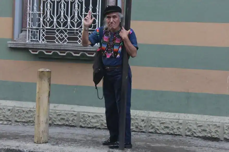 Campechano señor mayor con sombrero y ropa tradicional mexicana haciendo signo de paz en calle pintoresca, imagen para revista SoyMigrante.com sobre cultura y migración en México y América Latina. – SoyMigrante.com REVISTA
