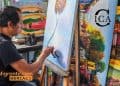 Migrant artist painting a blue-toned canvas at an easel, surrounded by colorful artworks; SoyMigrante.com MERCADO logo bottom left.