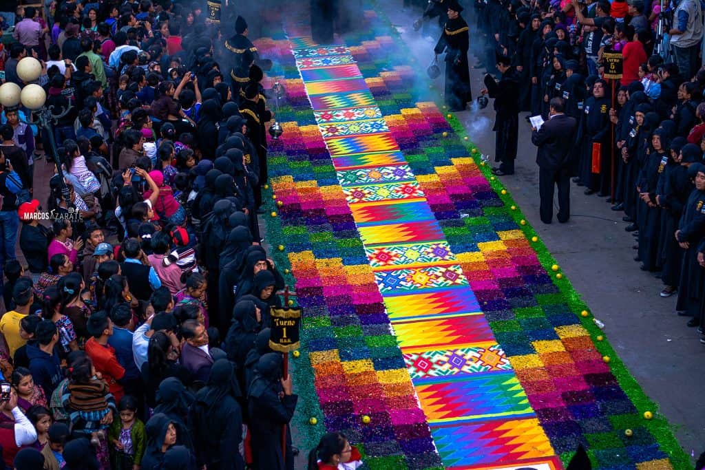 El aserrín se vuelve tejido de güipil, un lenguaje sin tiempo para el dueño del tiempo. – SoyMigrante.com REVISTA Colorido tapiz de papel picado y flor de cempasúchil en celebración tradicional mexicana, con multitud de personas participando en la fiesta del Día de Muertos. – SoyMigrante.com REVISTA
