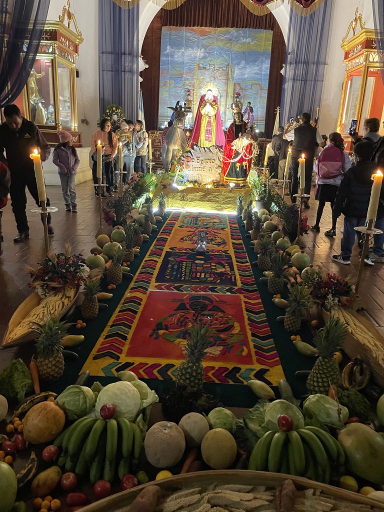 El fruto del trabajo se convierte en ofrenda piadosa alrededor de una alfombra que ayer fue árbol y mañana será recuerdo. San Pedro Las Huertas 2025 (Foto Michelle Gonzalez) – SoyMigrante.com REVISTA El fruto del trabajo se convierte en ofrenda piadosa alrededor de una alfombra que ayer fue árbol y mañana será recuerdo. San Pedro Las Huertas 2025 (Foto Michelle Gonzalez) – SoyMigrante.com REVISTA