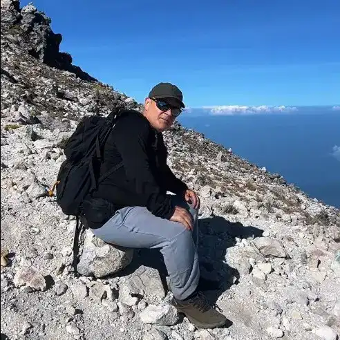 Explorador en la cima de una montaña con paisaje de nubes y mar al fondo, disfrutando de la naturaleza y la aventura. – SoyMigrante.com REVISTA