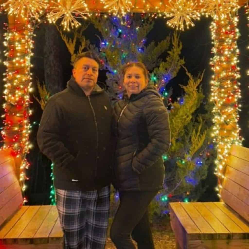 Familia disfrutando de luces navideñas en un entorno festivo, celebración de temporada en Países Andinos. Personas con vestimenta de invierno en decoraciones de Navidad, ambiente cálido y alegre. – SoyMigrante.com REVISTA