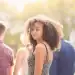 Chica joven con cabello rizado y sonrisa, en un entorno al aire libre con luz natural, representando temas de migración, juventud y diversidad en la comunidad latina.