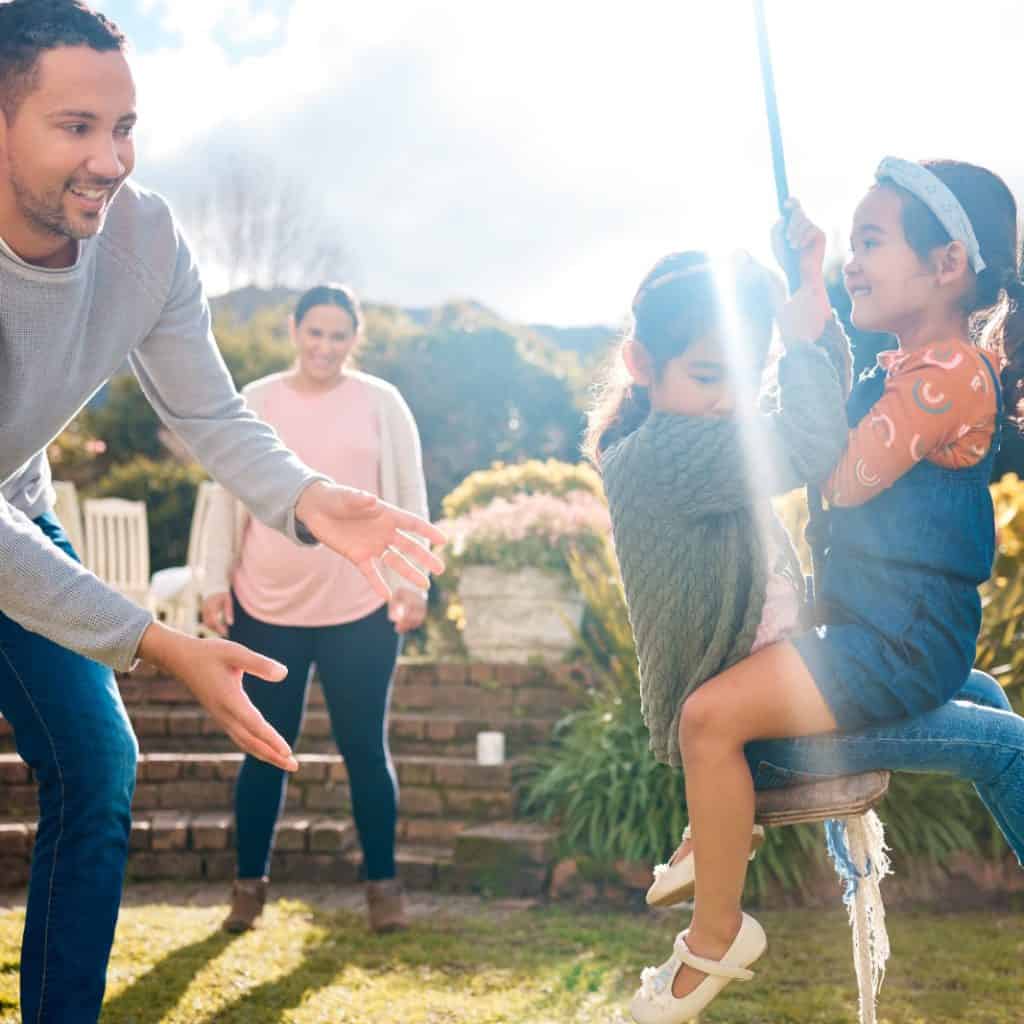 Diversión familiar en un jardín con niños jugando y adultos disfrutando del momento, promoviendo valores de migrantes y comunidad en SoyMigrante.com Revista.