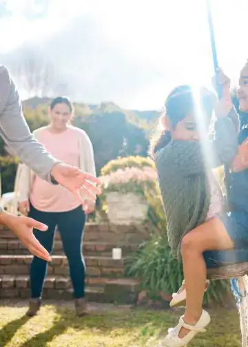 Diversión familiar en un jardín con niños jugando y adultos disfrutando del momento, promoviendo valores de migrantes y comunidad en SoyMigrante.com Revista. – SoyMigrante.com REVISTA