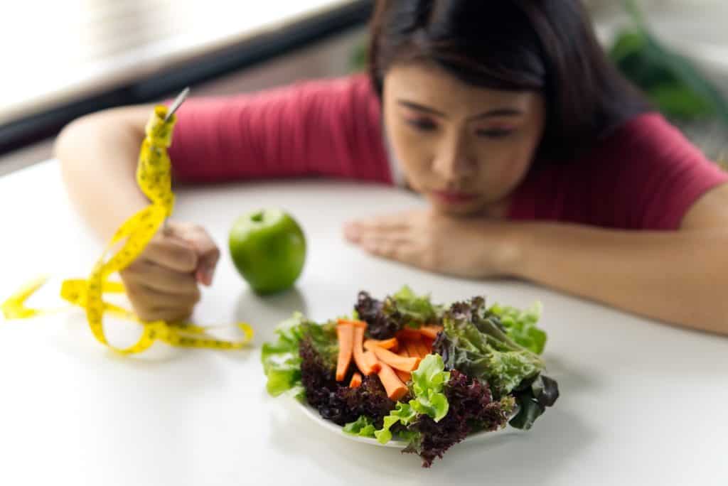 Imagen de mujer observando ensalada saludable con manzana y productos frescos, promoviendo vida sana, alimentación saludable y bienestar. – SoyMigrante.com REVISTA