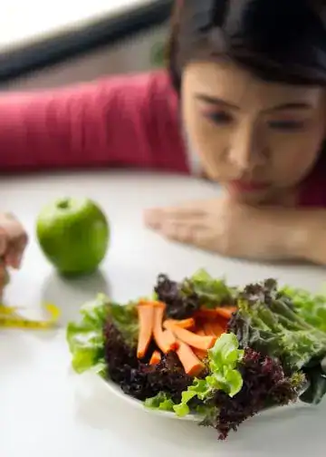 Trastornos alimenticios cómo detectarlos a tiempo y evitar que se agraven2 – SoyMigrante.com REVISTA Imagen de mujer observando ensalada saludable con manzana y productos frescos, promoviendo vida sana, alimentación saludable y bienestar. – SoyMigrante.com REVISTA