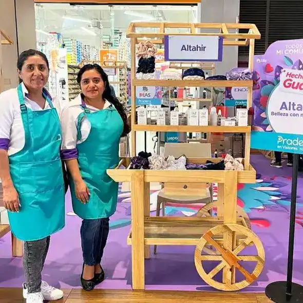 Accesible carrito de ventas con productos de belleza en tienda física, atendido por dos empleadas con delantales azul turquesa, en un entorno comercial colorido y moderno.