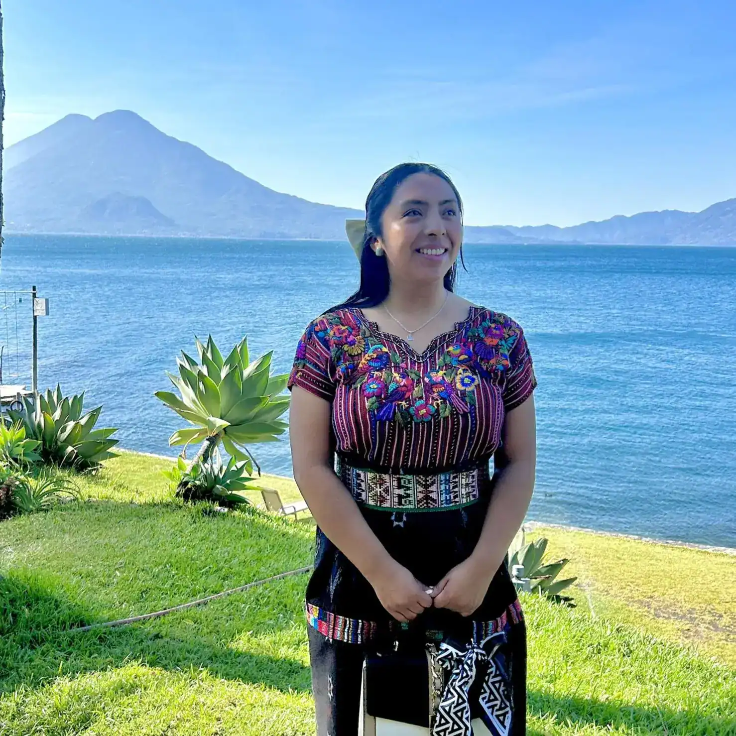 Mujer indígena con traje tradicional en un entorno natural frente a un lago y volcán, símbolo de cultura, identidad y orgullo en México.