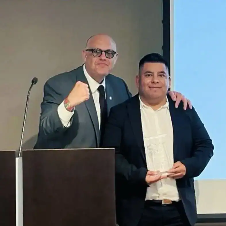 Álvaro y joven profesional en evento de la revista SoyMigrante.com REVISTA en un ambiente formal. – SoyMigrante.com REVISTA