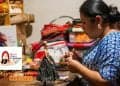 Muñecas que celebran la diversidad maya el sueño de Séfora – SoyMigrante.com REVISTA Guatemalan artisan sewing a doll in a busy fabric market, with 'SoyMigrante.com' logo in the corner