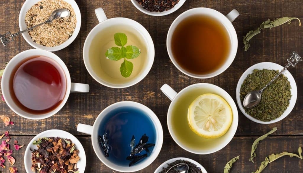 Tazas con diferentes infusiones y tés aromáticos en una mesa de madera, representando variedad y cultura en bebidas de café y té para inmigrantes y comunidad hispana. – SoyMigrante.com REVISTA