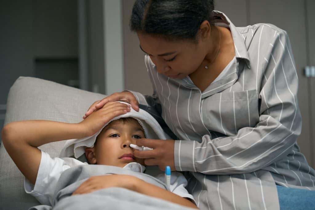 Enfermera atendiendo a un niño enfermo con fiebre en la clínica, atención médica infantil, cuidado y salud para migrantes y comunidades vulnerables. – SoyMigrante.com REVISTA