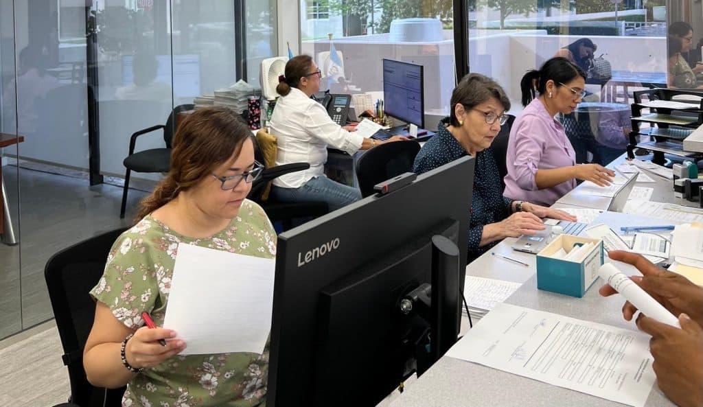Trabajadoras migrantes en oficina, desempeñando tareas administrativas y revisando documentos en un entorno laboral dedicado a la comunidad migrante en la revista SoyMigrante.com.
