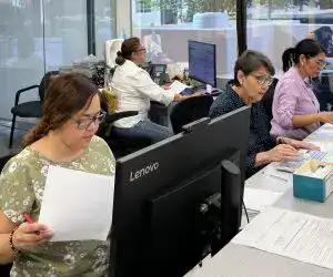 Trabajadoras migrantes en oficina, desempeñando tareas administrativas y revisando documentos en un entorno laboral dedicado a la comunidad migrante en la revista SoyMigrante.com.