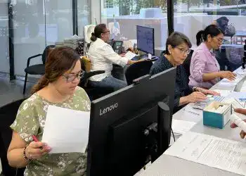 Trabajadoras migrantes en oficina, desempeñando tareas administrativas y revisando documentos en un entorno laboral dedicado a la comunidad migrante en la revista SoyMigrante.com.