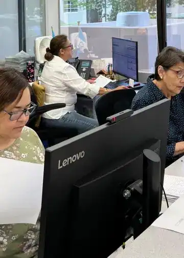 Trabajadoras migrantes en oficina, desempeñando tareas administrativas y revisando documentos en un entorno laboral dedicado a la comunidad migrante en la revista SoyMigrante.com. – SoyMigrante.com REVISTA