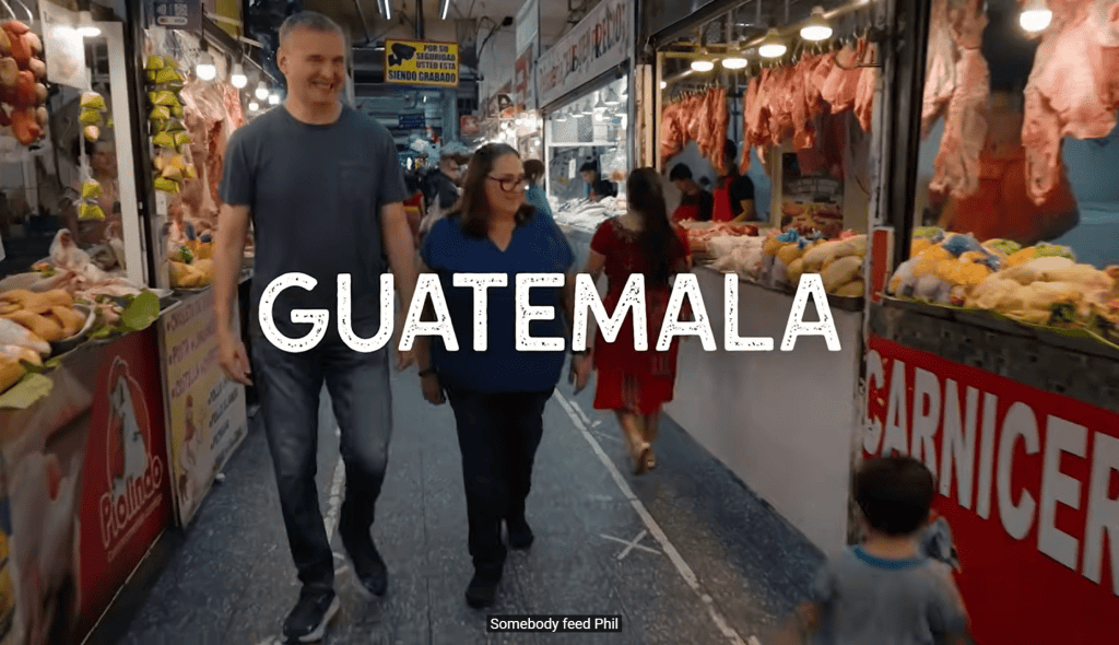 Varias personas caminando en un mercado de Guatemala, rodeados de puestos de carne y productos frescos, resaltando la cultura y gastronomía guatemalteca.