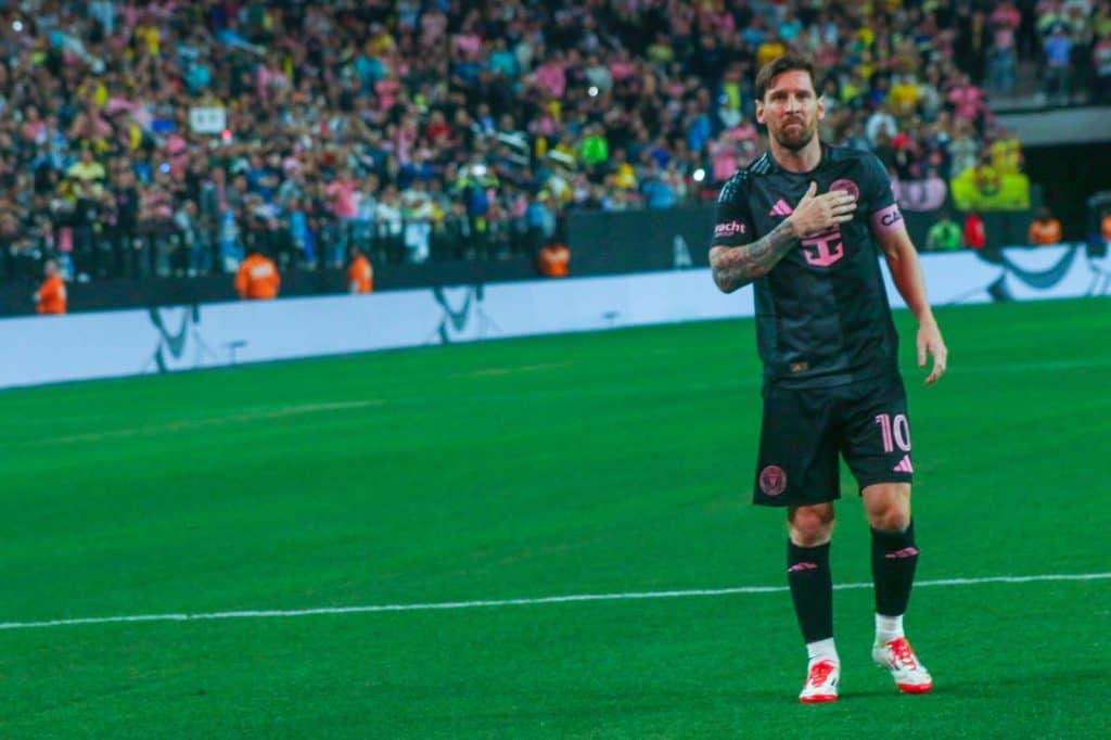 Goleador del fútbol internacional, jugador en la cancha durante partido, celebración por gol, evento deportivo, futbolista profesional ataviado con uniforme negro y rosa, estadio lleno de espectadores, momento de victoria.