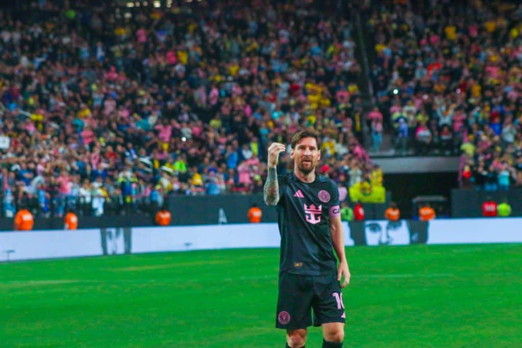 Futbolista en el campo celebrando con público en las gradas durante un partido de fútbol.