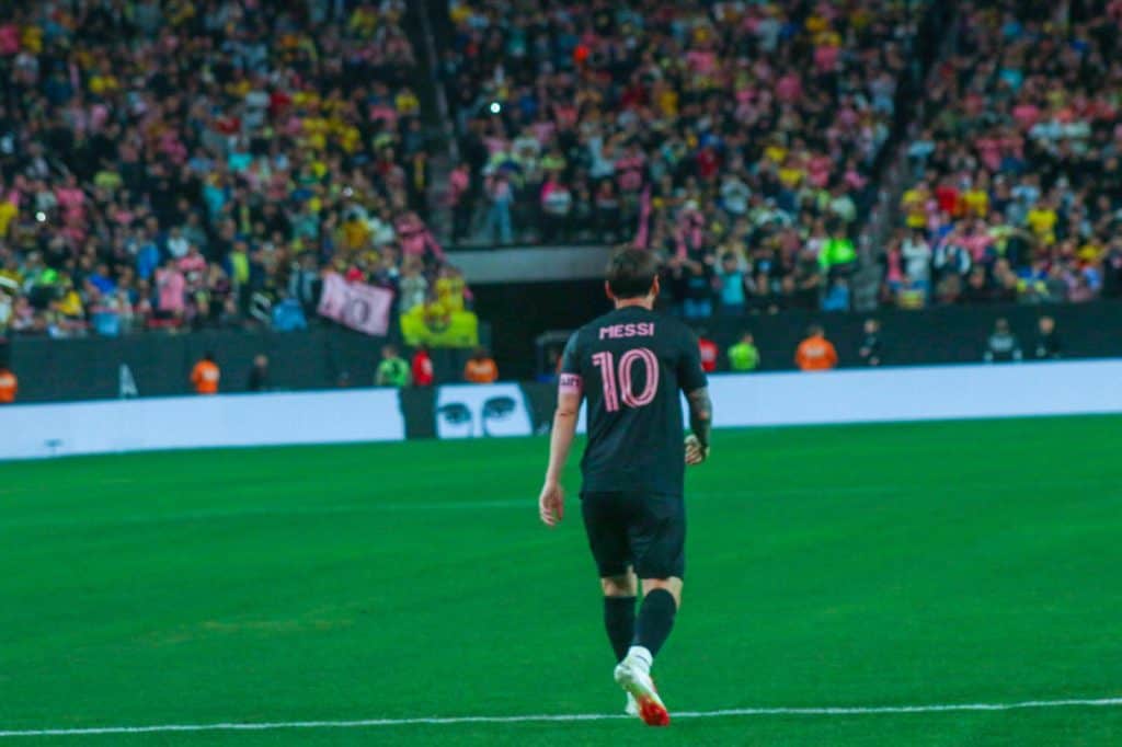 Messi jugando en un partido de fútbol en un estadio con gran afluencia de público, promoviendo la pasión por el deporte y el talento futbolístico.
