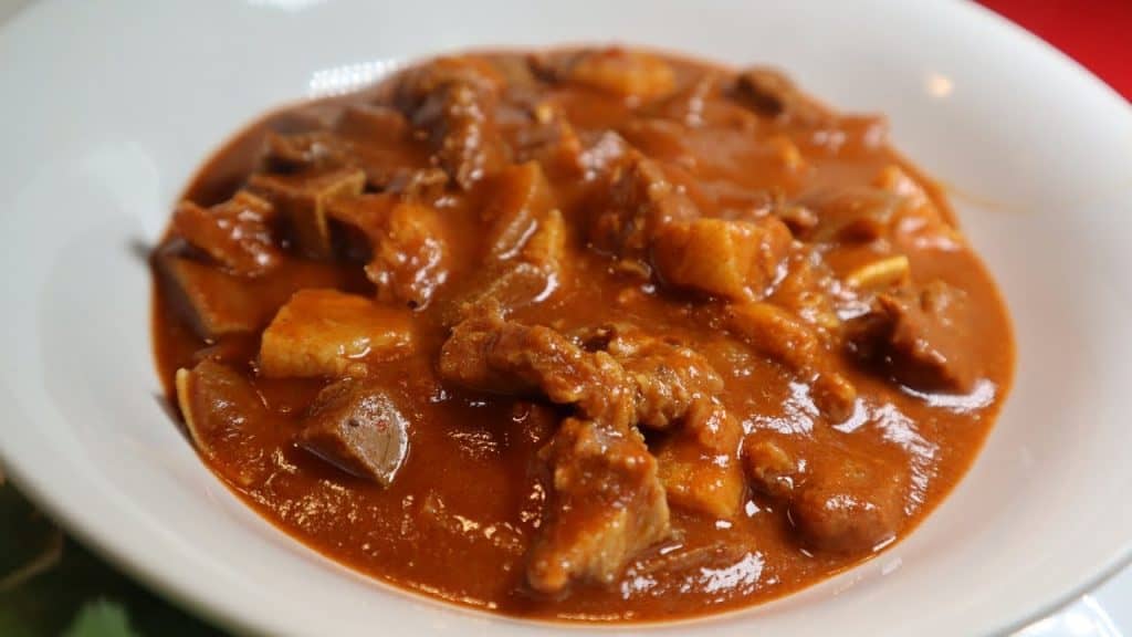 Jugos de carne guisada con salsa espesa y trozos de carne en plato blanco para recetas mexicanas o latinoamericanas.