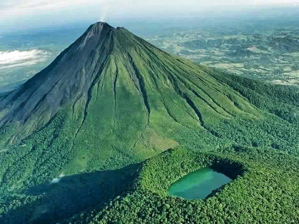 Vulcano volcánico cubierto de vegetación con un cráter y un pequeño lago, paisaje natural en Guatemala, símbolo de la belleza y los desafíos del medio ambiente en América Central.