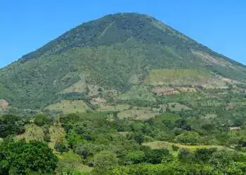 Cerro volcánico verde con cielo claro, paisaje natural y agrícola en primer plano, símbolo de biodiversidad y recursos en México.