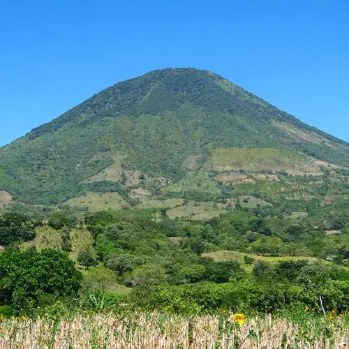 Cerro volcánico verde con cielo claro, paisaje natural y agrícola en primer plano, símbolo de biodiversidad y recursos en México.