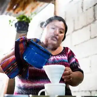 Mujer migrante preparando café tradicional en su hogar, destacando cultura y experiencias de la comunidad migrante en América Latina. – SoyMigrante.com REVISTA