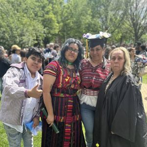 Diversas personas en celebración de graduation en un parque, mostrando orgullo y alegría, con árboles verdes y una multitud en el fondo, en un evento cultural y de reconocimiento académico.