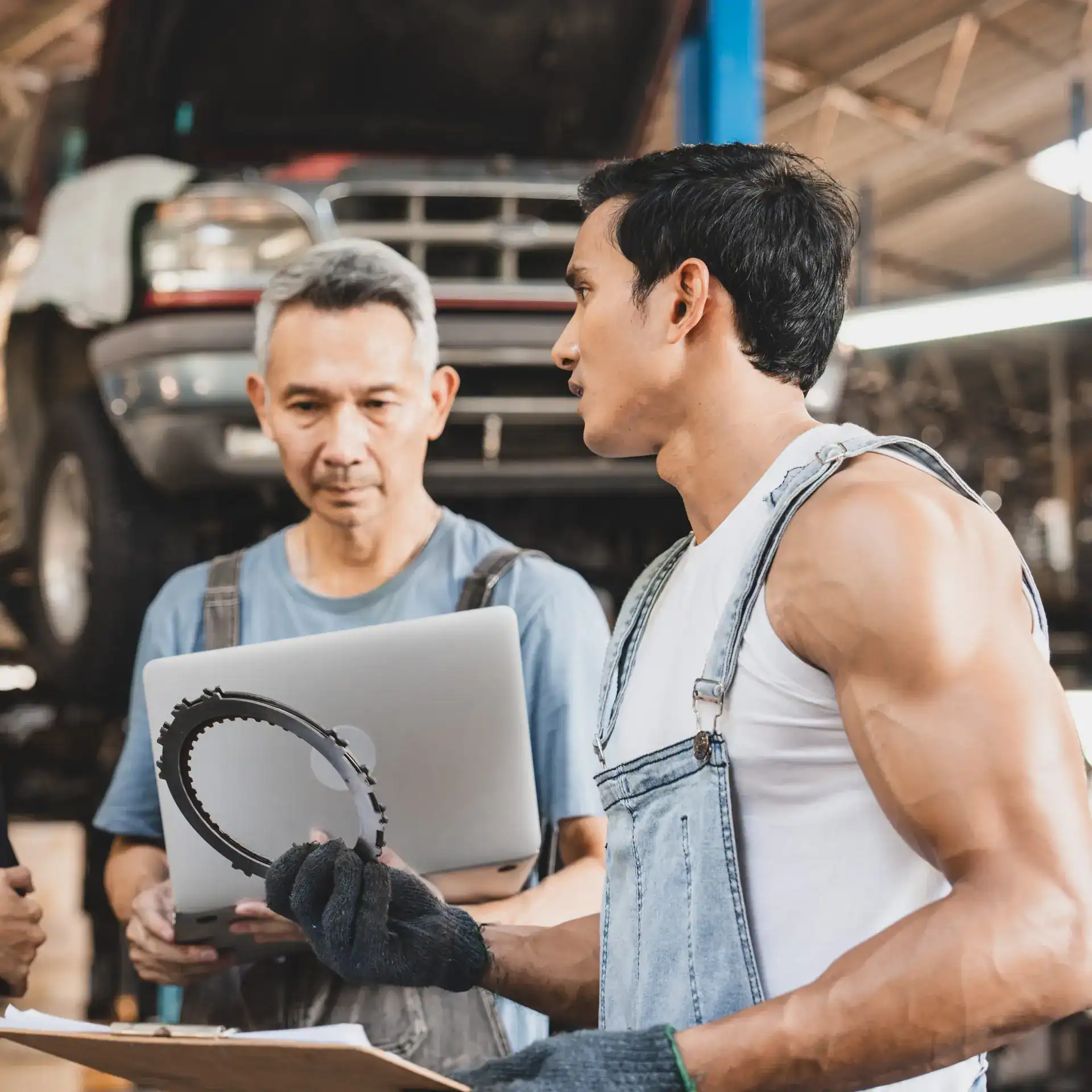 Trabajadores mecánicos en taller consultando reparación, con coche elevándose en segundo plano, enfocados en mantenimiento automotriz, concepto de empleo y trabajo en el sector automotriz.