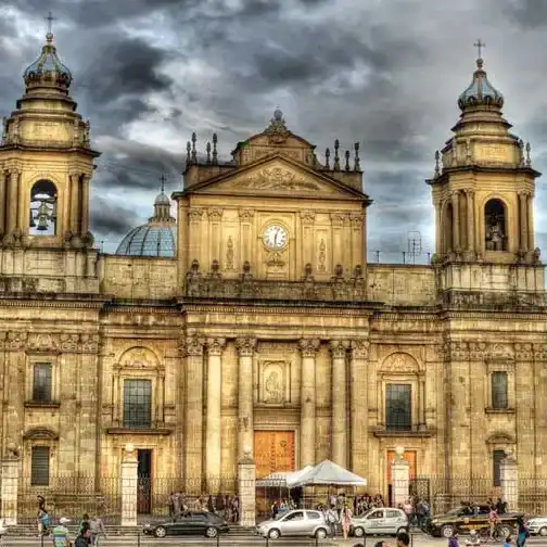 Majestuosa fachada de una catedral colonial en una ciudad histórica, con torres gemelas y un cielo nublado, representando arquitectura religiosa y patrimonio cultural en Latinoamérica. – SoyMigrante.com REVISTA