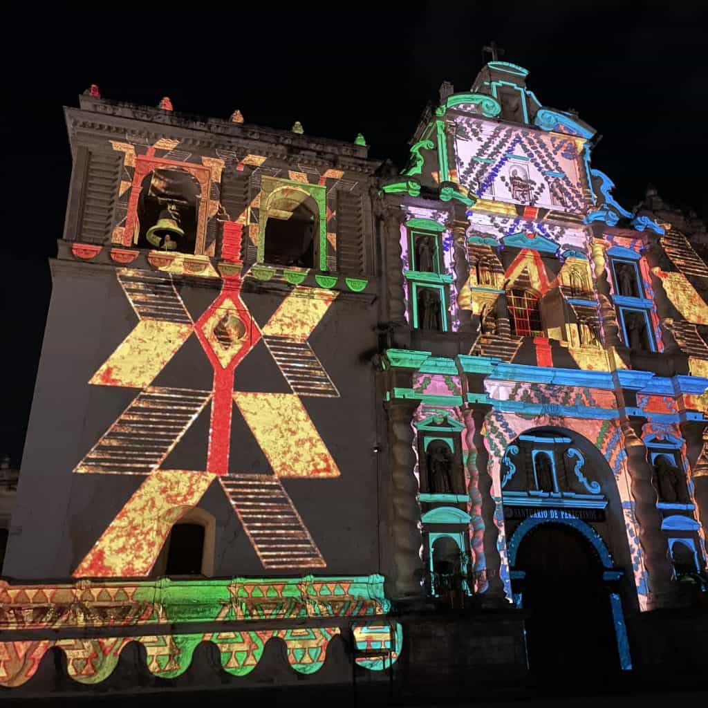Colorido espectáculo de proyección en una iglesia histórica en Mexicali, resaltando el arte y cultura migrante en México con luz vibrante y efectos visuales impactantes durante la noche.