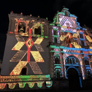 Colorido espectáculo de proyección en una iglesia histórica en Mexicali, resaltando el arte y cultura migrante en México con luz vibrante y efectos visuales impactantes durante la noche. – SoyMigrante.com REVISTA