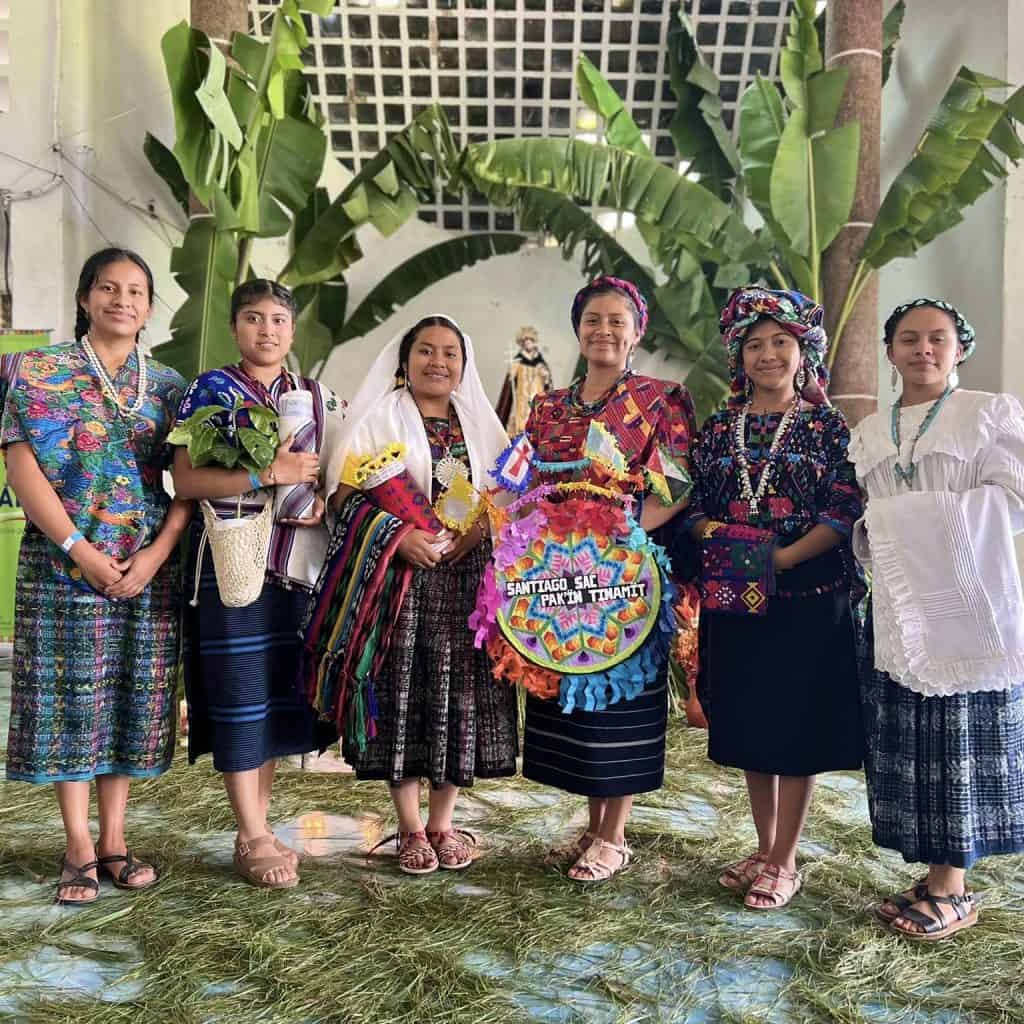 Coloridas mujeres indígenas en vestimenta tradicional durante celebración cultural en un entorno natural.